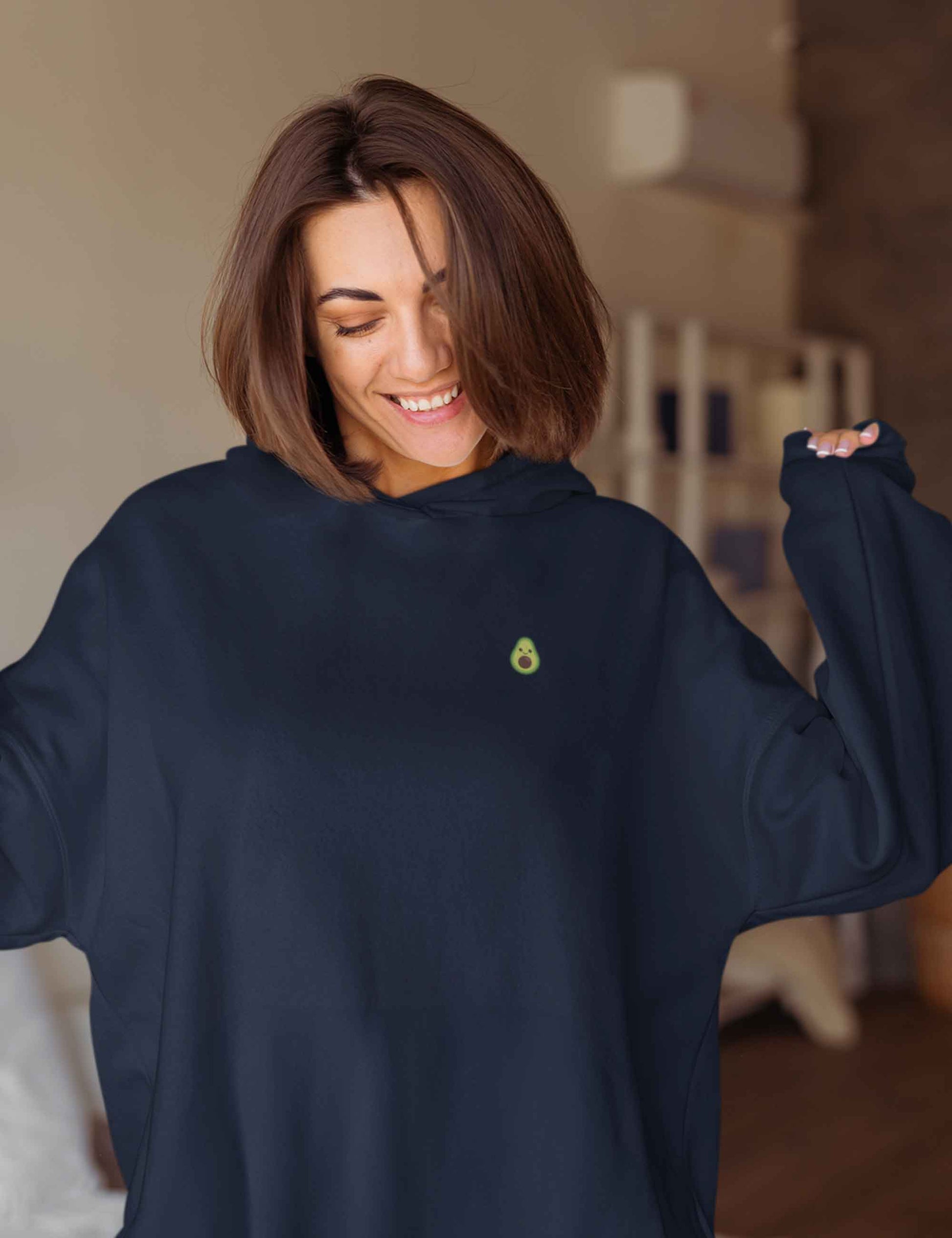 Lächelnde Frau mit einem Oversized-Hoodie in dunkelblau mit süßen kleinen Avocinchen auf der Brust.