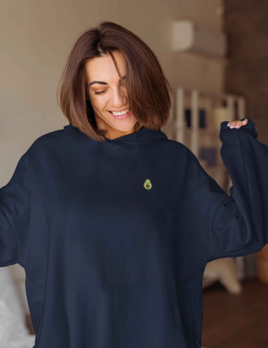 Lächelnde Frau mit einem Oversized-Hoodie in dunkelblau mit süßen kleinen Avocinchen auf der Brust.