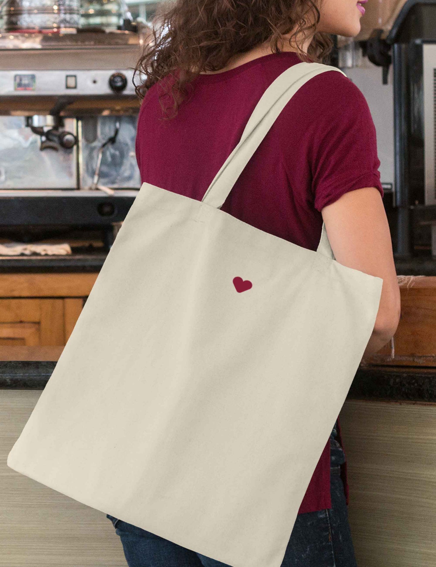 Frau trägt einen Baumwollbeutel naturfarben, mit Bodenfalte, langen Henkeln zum besseren Tragen und einem kleinen weichen Herz aus Flock