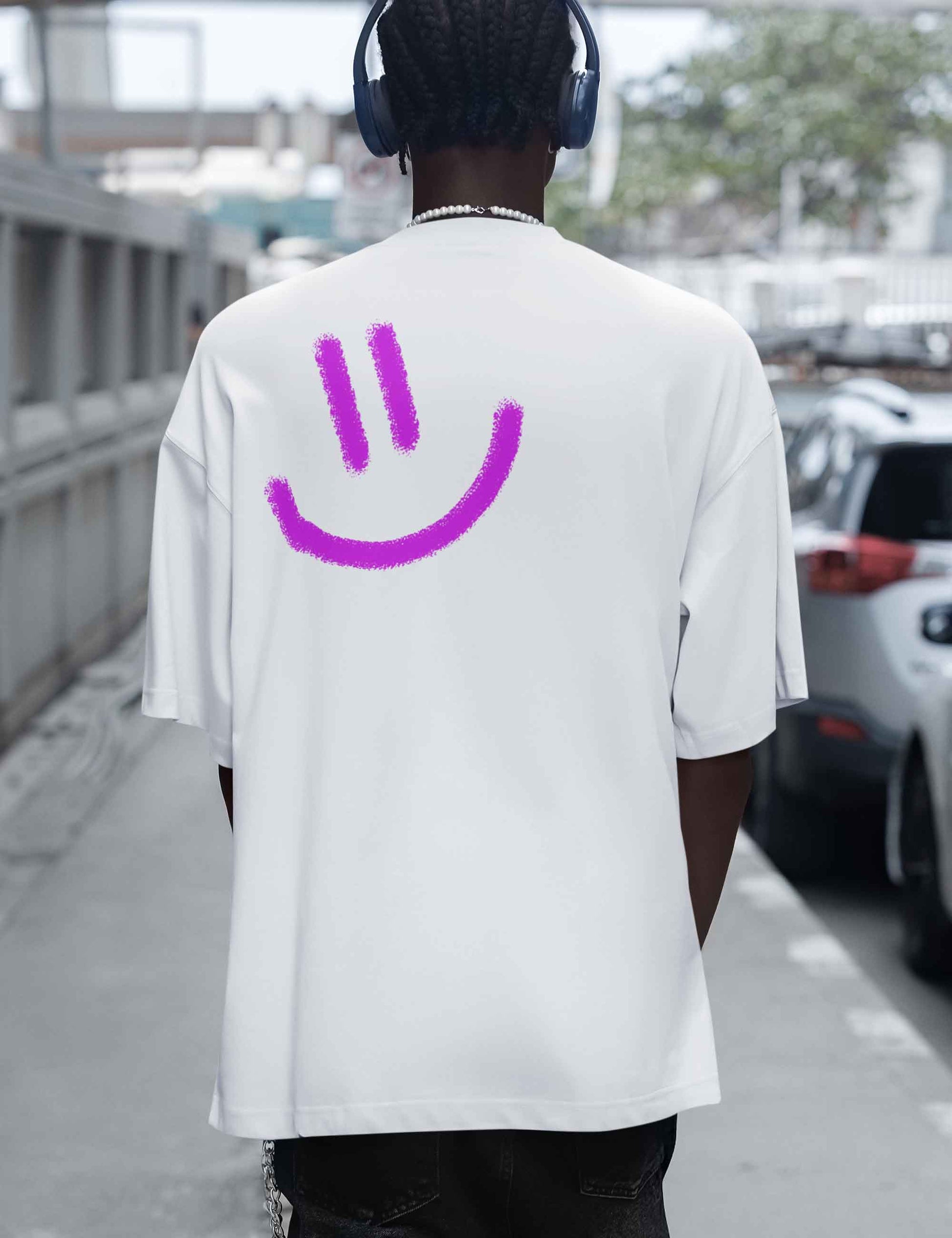 Mann mit lockerem oversized T-Shirt in schlichtem Weiß mit richtig großem gespraytem pinken Smiley auf der Rückseite