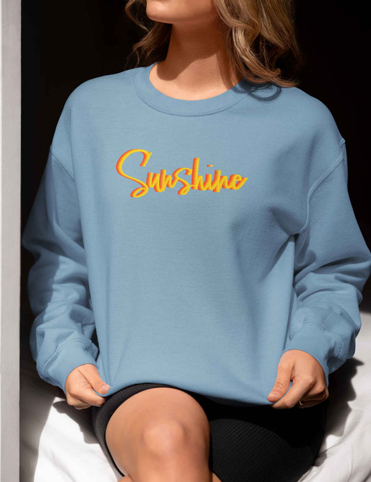 Frau trägt einen Oversized geschnittenen Sweater in tollem Graublau mit dem Schriftzug Sunshine in knalligen, sonnigen Farben