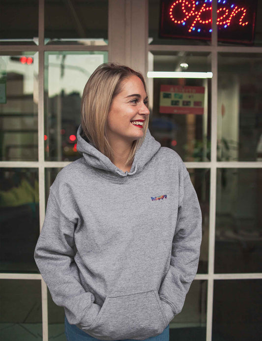 Lächelnde Frau mit grau meliertem Hoodie mit kleinem happy in bunten Farben auf der Front