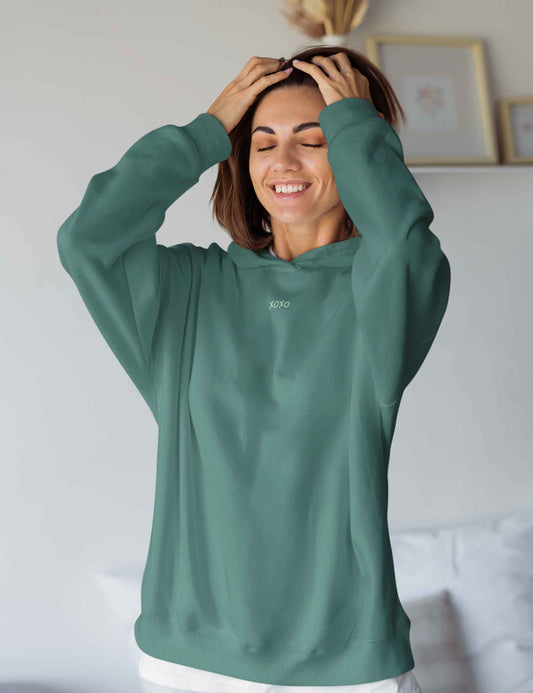 Frau trägt einen Hoodie: Ein pastellfarbenes xoxo macht diesen ansonsten schlichten oversized Hoodie in einem Petrolgrün zu einem stylischen Alltagsbegleiter.